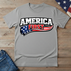 Sport Gray t-shirt with 'America First' graphic on a wooden surface with jeans and an American flag.